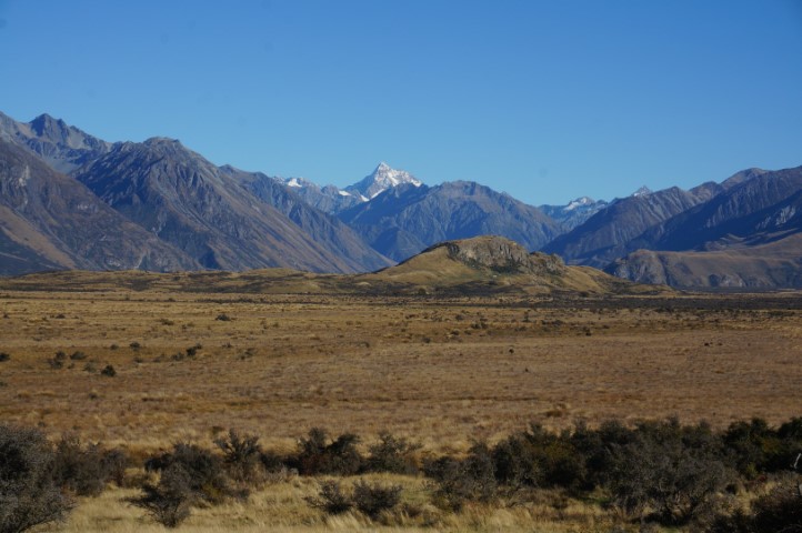 Picture of an alone peak in the middle of flatland surrounded by mountains